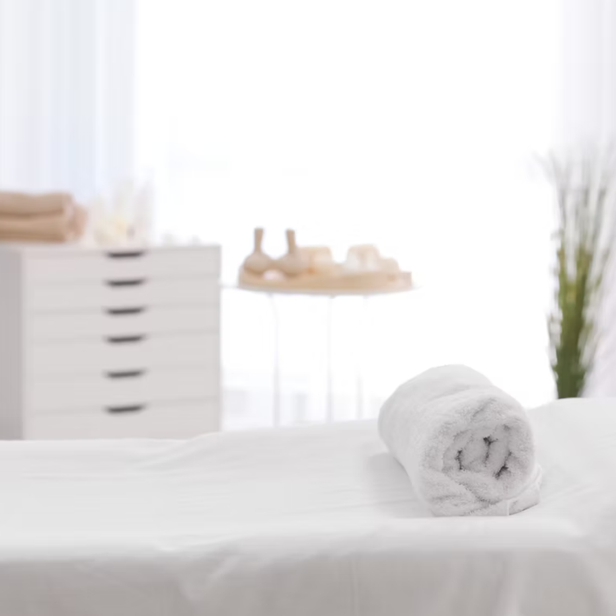 massage treatment bed with white sheets and a white rolled up towel