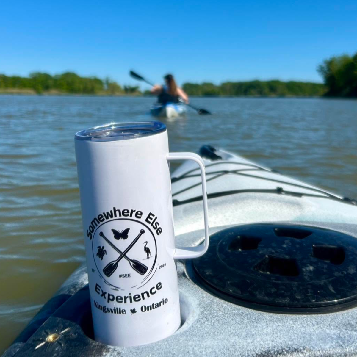 To go thermos with Somewhere Else Experience logo sitting in the cup holder of a kayak on the water