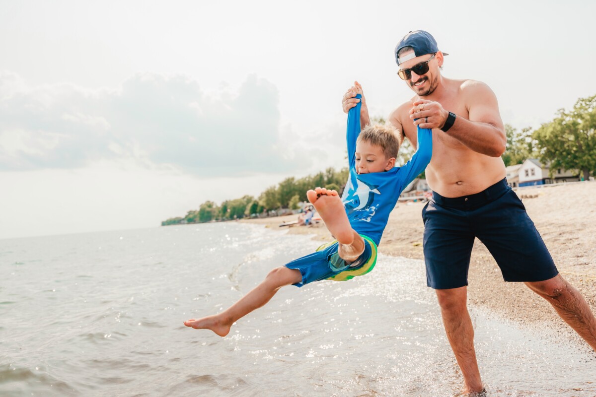 Dad swings his son into lake along sandy beach