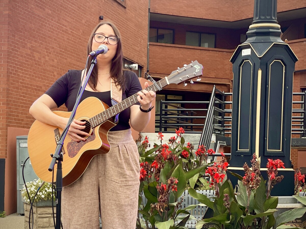 A performer sings and plays guitar on an outdoor stage